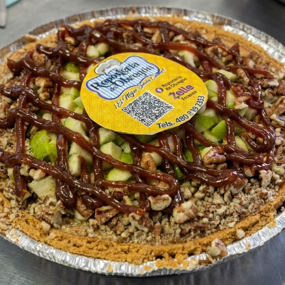 Round apple pecan pie in a foil tin, topped with chopped nuts and chocolate drizzle, with a yellow bakery label.