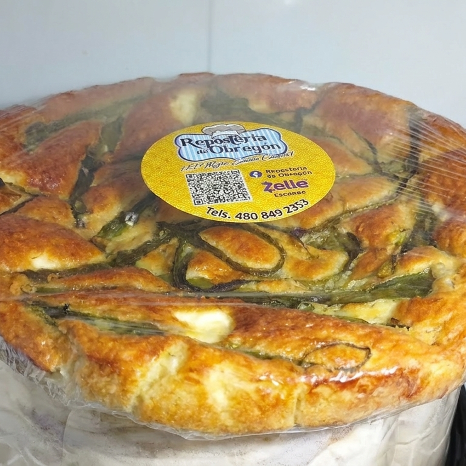 Golden savory vegetable pie with green filling, wrapped in plastic and labeled, displayed on a refrigerated bakery shelf.