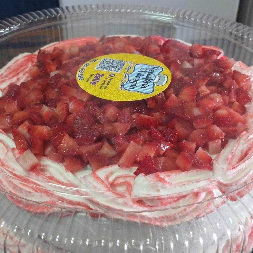 Round strawberry-topped cake with swirled pink-and-white frosting in a clear plastic bakery container.