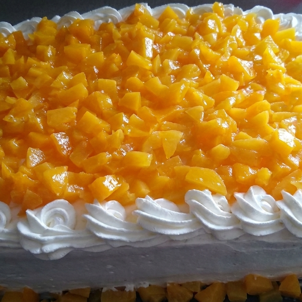 Rectangular cream-covered cake topped with diced golden fruit and bordered by piped whipped cream rosettes.